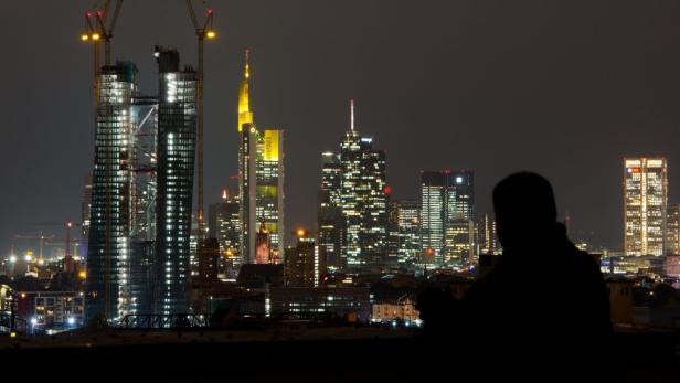 Auf die nächtliche Bankenskyline von Frankfurt am Main blickt dieser Mann am 11.10.2012 vom Dach eines Hochhauses aus. Dabei dominiert der Neubau der Europäischen Zentralbank (EZB, links) bereits vor seiner Fertigstellung die anderen Bankhäuser. Rechts neben der EZB sind die Commerzbank, die Helaba sowie die Türme der Deutschen Bank zu sehen. Foto: Boris Roessler dpa +++(c) dpa - Bildfunk+++