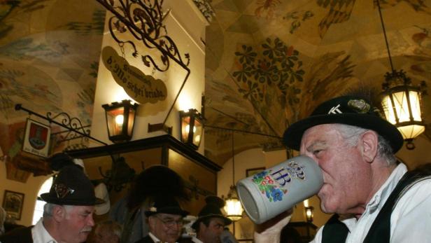 Männer in Tracht sitzen in einem traditionellen bayerischen Lokal und trinken Bier.