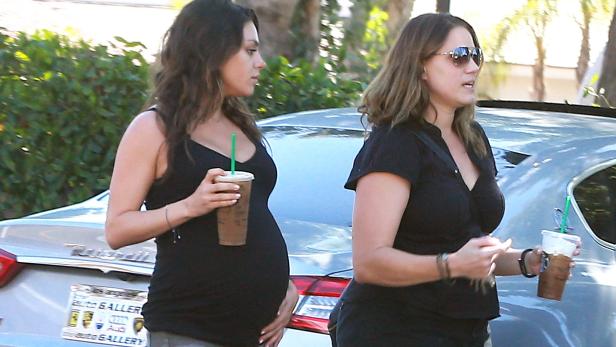 Die schwangere Mila Kunis mit einem Getränk in der Hand, neben einer Freundin stehend.