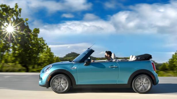 Ein türkisfarbenes Mini Cabrio fährt auf einer Landstraße.