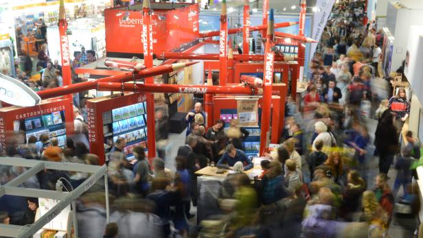 Viele Menschen besuchen einen Stand mit übergroßen Bleistiftdekorationen auf einer Buchmesse.