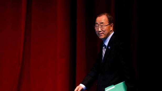 Ban Ki-moon geht mit einer grünen Mappe in der Hand vor einem roten Vorhang entlang.