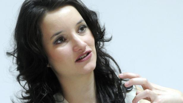 Eine Frau mit dunklen, gewellten Haaren schaut zur Seite.