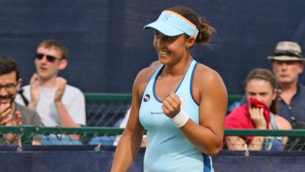 Eine Tennisspielerin jubelt auf dem Platz, während Zuschauer im Hintergrund applaudieren.