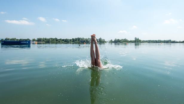 Beine ragen aus dem Wasser eines Sees, während eine Person einen Kopfsprung macht.