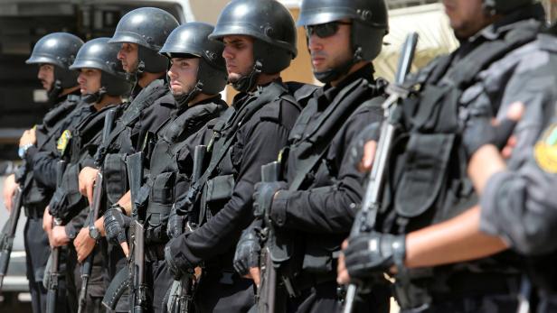 Eine Reihe von Polizisten in schwarzer Uniform und Helmen stehen mit Gewehren in einer Reihe.