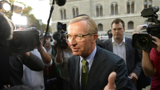 Ein Mann im Anzug wird von Fernsehkameras umringt.