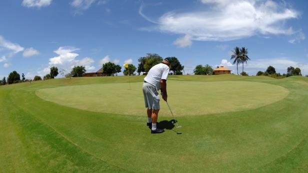 Ein Mann puttet auf einem Golfplatz unter blauem Himmel.