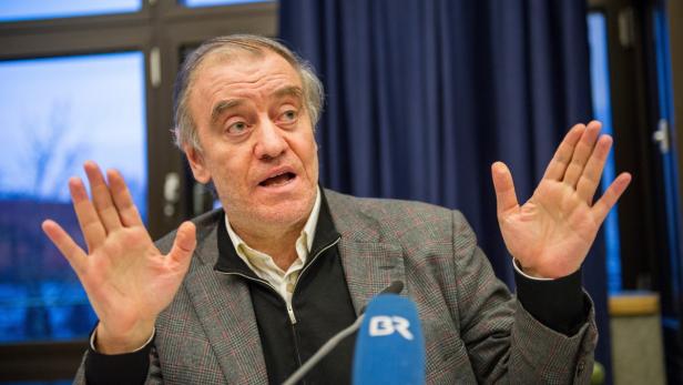 Ein Mann gestikuliert während einer Rede vor einem Mikrofon.