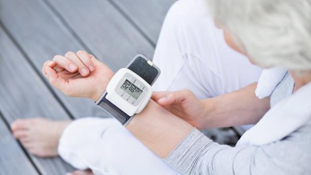 Eine ältere Frau misst ihren Blutdruck mit einem Handgelenk-Blutdruckmessgerät.