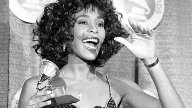Whitney Houston hält freudestrahlend eine Grammy-Trophäe in der Hand.