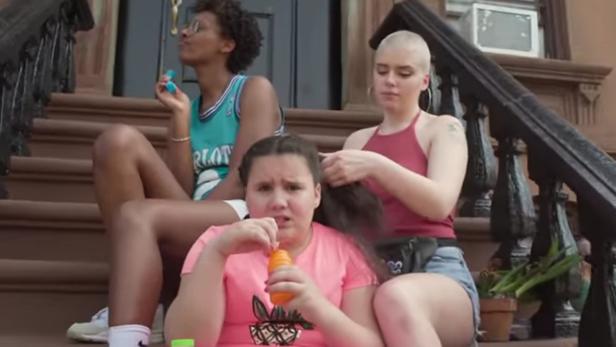 Drei junge Frauen sitzen auf einer Treppe und machen Seifenblasen oder flechten Zöpfe.