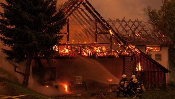Ein brennendes Haus wird von Feuerwehrleuten mit Wasser bespritzt.