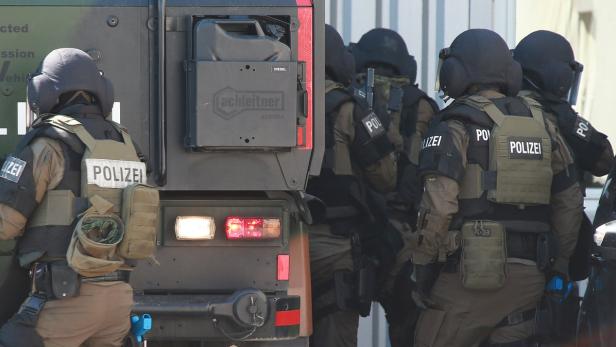 Eine Gruppe Polizisten in voller Montur steht neben einem gepanzerten Fahrzeug.