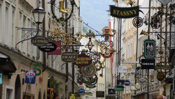 Eine Gasse mit vielen Schildern von Geschäften und Restaurants in Salzburg.