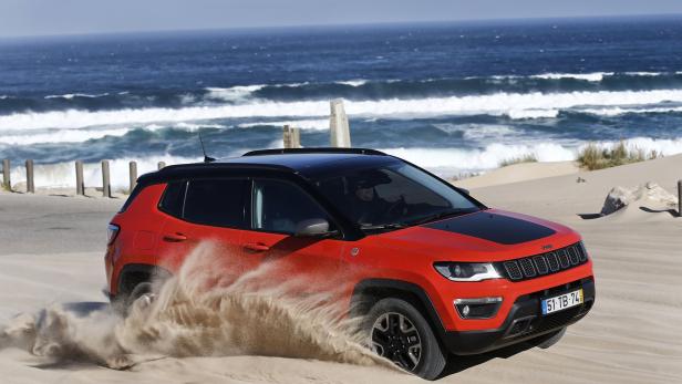 Ein roter Jeep Compass fährt durch den Sand am Strand.