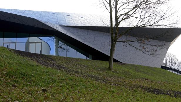 Ein modernes Gebäude mit einer Fassade aus grauen Platten und einem Baum im Vordergrund.