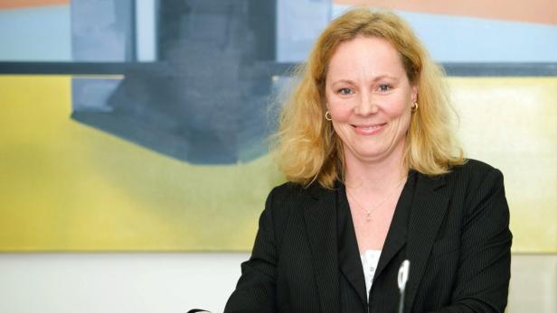 Eine blonde Frau lächelt vor einem abstrakten Gemälde.