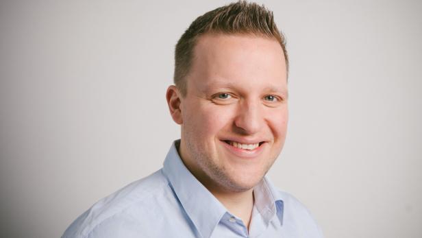 Ein lächelnder Mann mit hellblauem Hemd vor einem hellen Hintergrund.