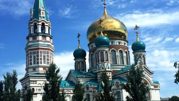 Die Mariä-Entschlafens-Kathedrale in Omsk mit goldenen Kuppeln unter blauem Himmel.