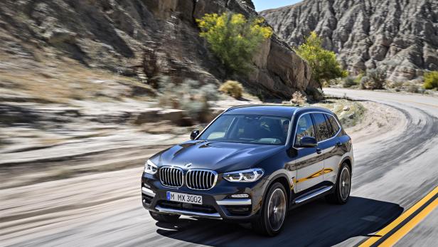 Ein schwarzer BMW X3 fährt auf einer kurvenreichen Straße durch eine hügelige Landschaft.