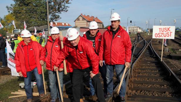 Eine Gruppe von Bauarbeitern steht auf einem Bahngleis mit einem Schild „Tusk Oszust“.
