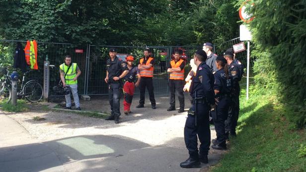 Eine Gruppe von Polizisten und Bauarbeitern steht vor einem Bauzaun.