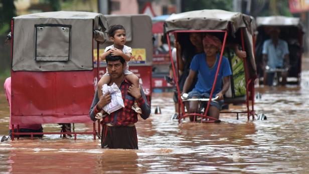 Ein Inder watet mit seinem Sohn durch das Hochwasser in Guwahati.