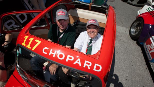 Zwei Männer sitzen in einem roten Oldtimer mit der Aufschrift „Chopard“.
