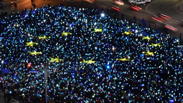 Eine große Menschenmenge hält leuchtende Handys und rumänische Flaggen in die Höhe.