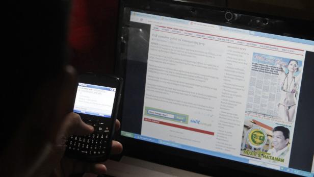 epa03400460 A Filipino journalist reads smartphone messages while using a laptop computer with internet features at a local district press office in Quezon City, east of Manila, Philippines, 17 September 2012. Local media reported that Philippine President Benigno Aquino III signed into law on 12 September the Republic Act 10175 or the Cybercrime Prevention Act of 2012, a measure aimed at punishing online libel and crimes or offenses committed using the internet. EPA/ROLEX DELA PENA