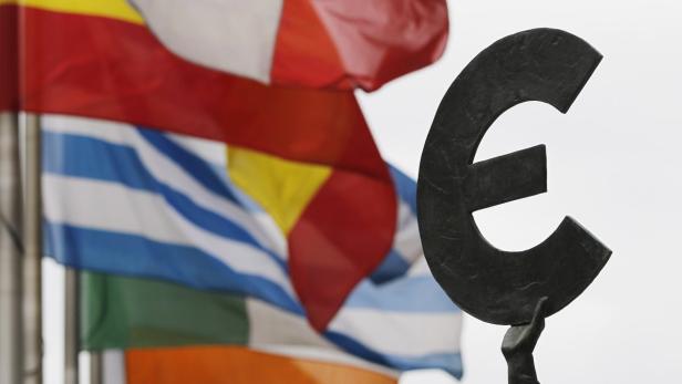 Eine Euro-Skulptur vor einer Reihe von EU-Flaggen.