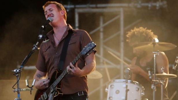 Ein Sänger spielt Gitarre und singt in ein Mikrofon, während ein Schlagzeuger im Hintergrund spielt.