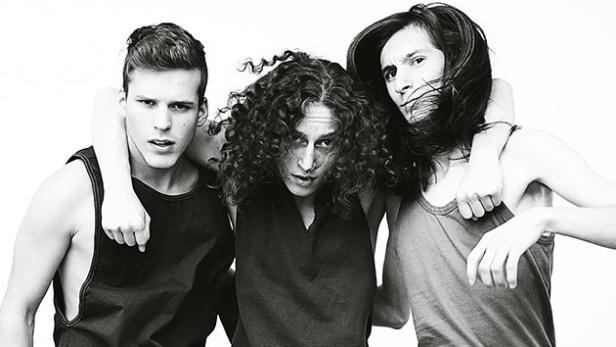 Drei junge Menschen stehen eng nebeneinander, in Schwarz-Weiß gehalten.