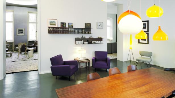 Ein Esszimmer mit einem Holztisch und violetten Sesseln unter bunten Lampen.