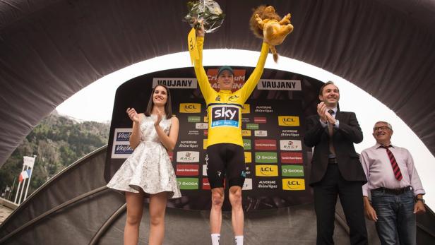 Ein Radrennfahrer im gelben Trikot feiert seinen Sieg auf dem Podium.