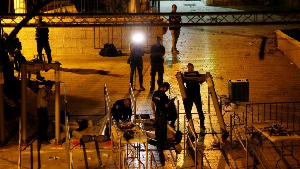 Polizisten bauen am Abend Sicherheitsschleusen auf einer Straße auf.