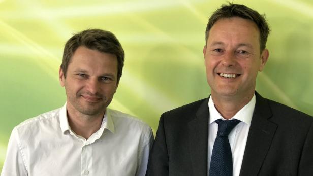 Zwei Männer posieren vor einem hellgrünen Hintergrund.