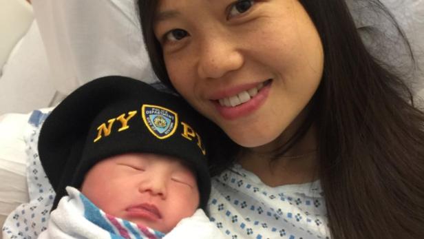 Eine Frau hält ein Neugeborenes mit einer Mütze des New York Police Department im Arm.