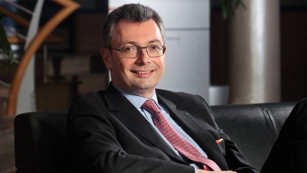 Dr. Alexander Picker Ein lächelnder Mann mit Brille und Anzug sitzt auf einem schwarzen Ledersofa.