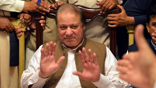 Ein Mann in Weste hebt seine Hände vor einer Gruppe von Menschen.