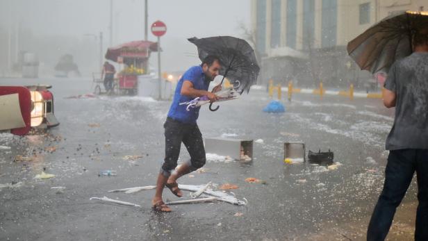 Ein Mann kämpft mit einem Regenschirm gegen einen Hagelsturm auf einer überschwemmten Straße.