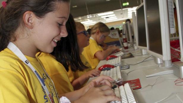 Mehrere Kinder sitzen an Computern und tippen auf Tastaturen.