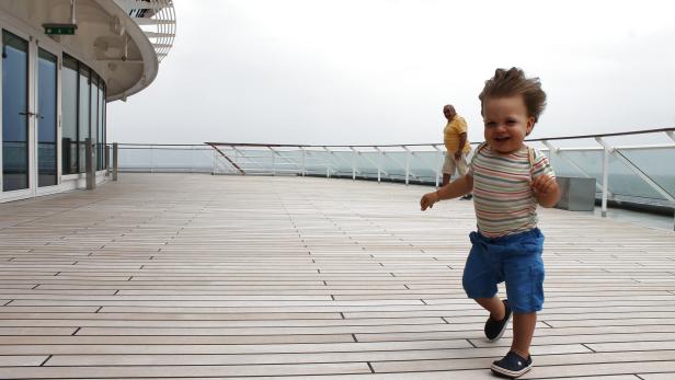 Ein lachender Junge rennt auf dem Deck eines Schiffes.