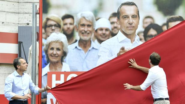 Zwei Männer enthüllen ein Wahlplakat mit dem Porträt eines Politikers und weiteren Personen.