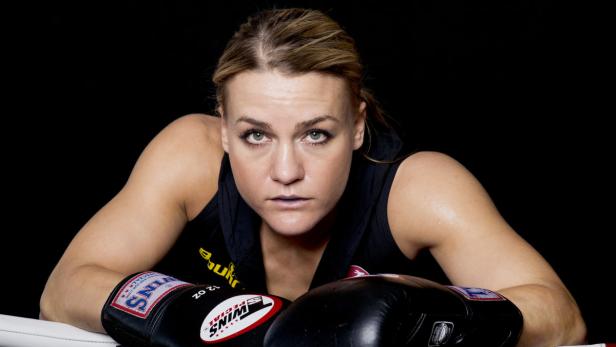Eine Boxerin mit Boxhandschuhen ruht sich im Ring aus.