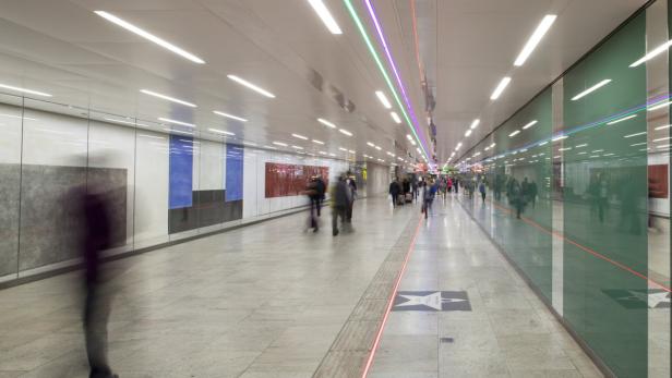 Menschen gehen durch einen hell erleuchteten U-Bahnhof mit Kunst an den Wänden.