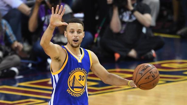 Stephen Curry winkt mit einem Basketball in der Hand.