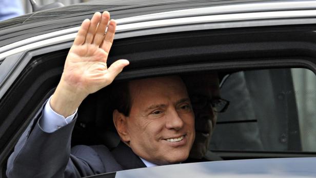 Silvio Berlusconi winkt aus dem Fenster eines Autos.