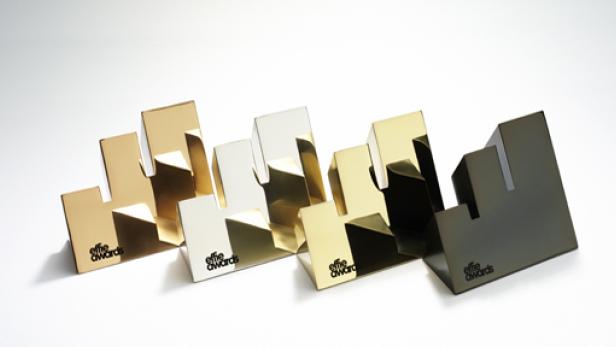 Mehrere Effie Awards in Gold, Silber und Bronze stehen auf einer weißen Oberfläche.